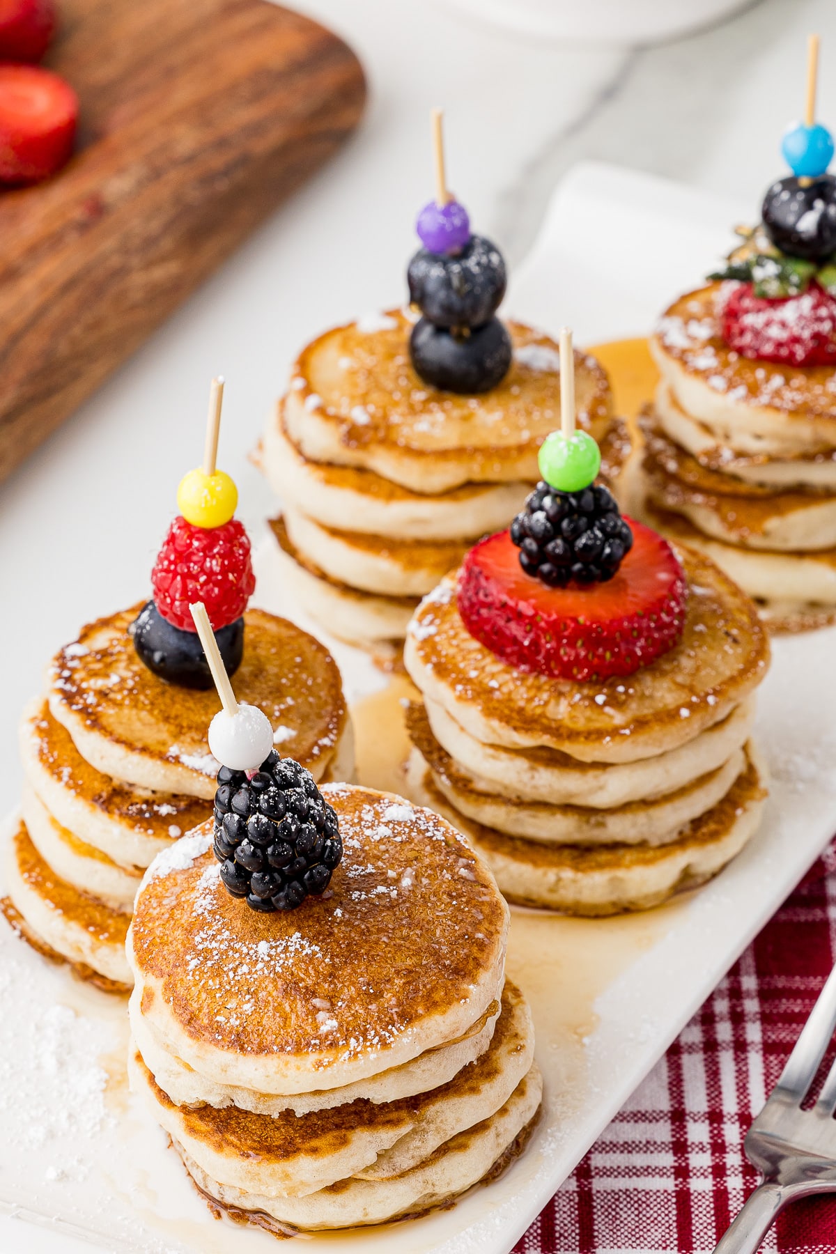 Stacked mini pancakes with skewers and mixed berries on a serving plate