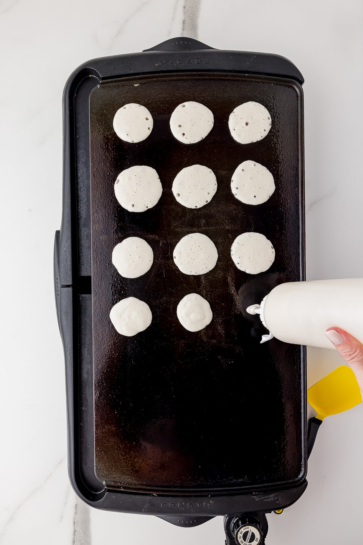 large griddle with a squeeze bottle of pancake batter being squeezed