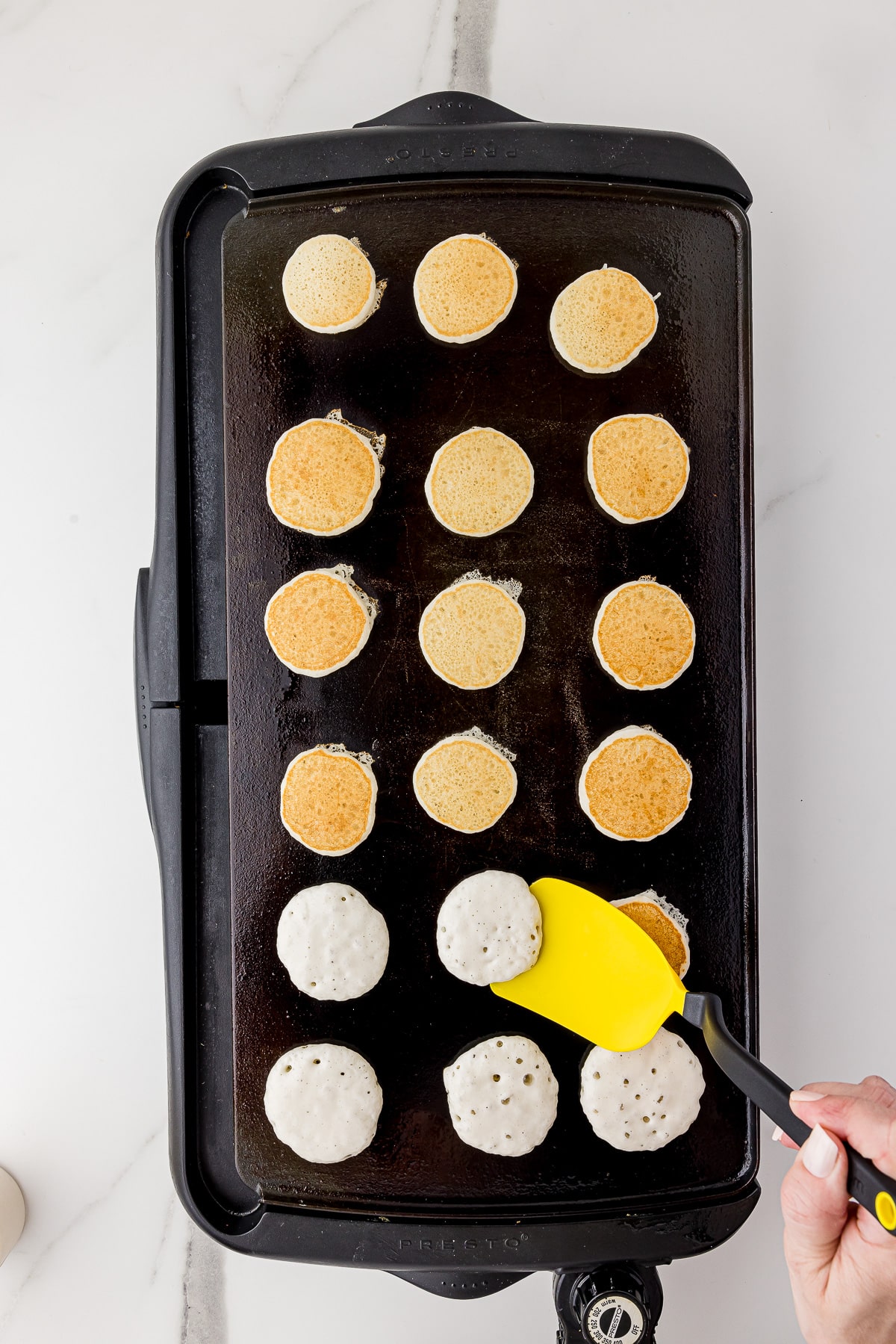 large griddle with 18 mini pancakes being cooked