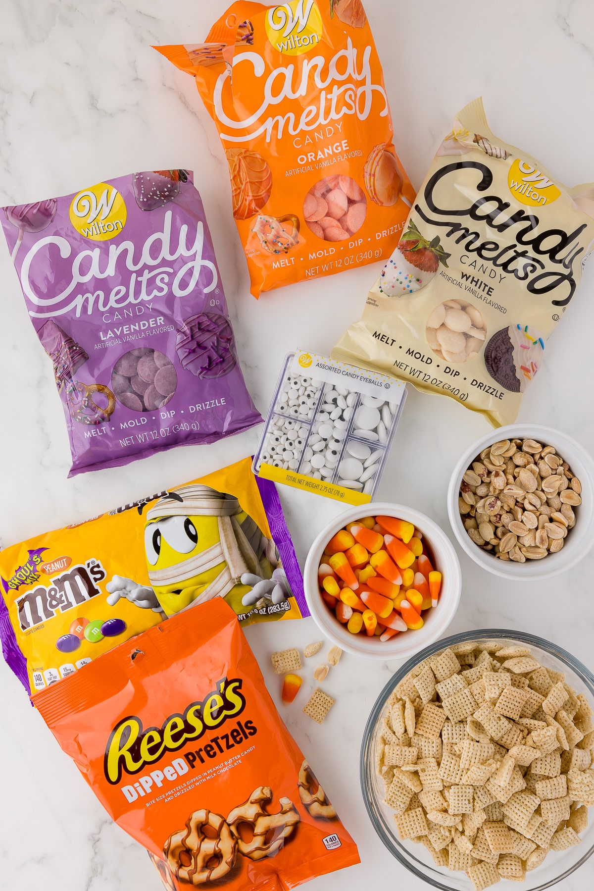ingredients for monster munch, wilton candy melts, candy eyes, m&m's, reese's dipped pretzels, candy corn, chex cereal, and shelled peanuts