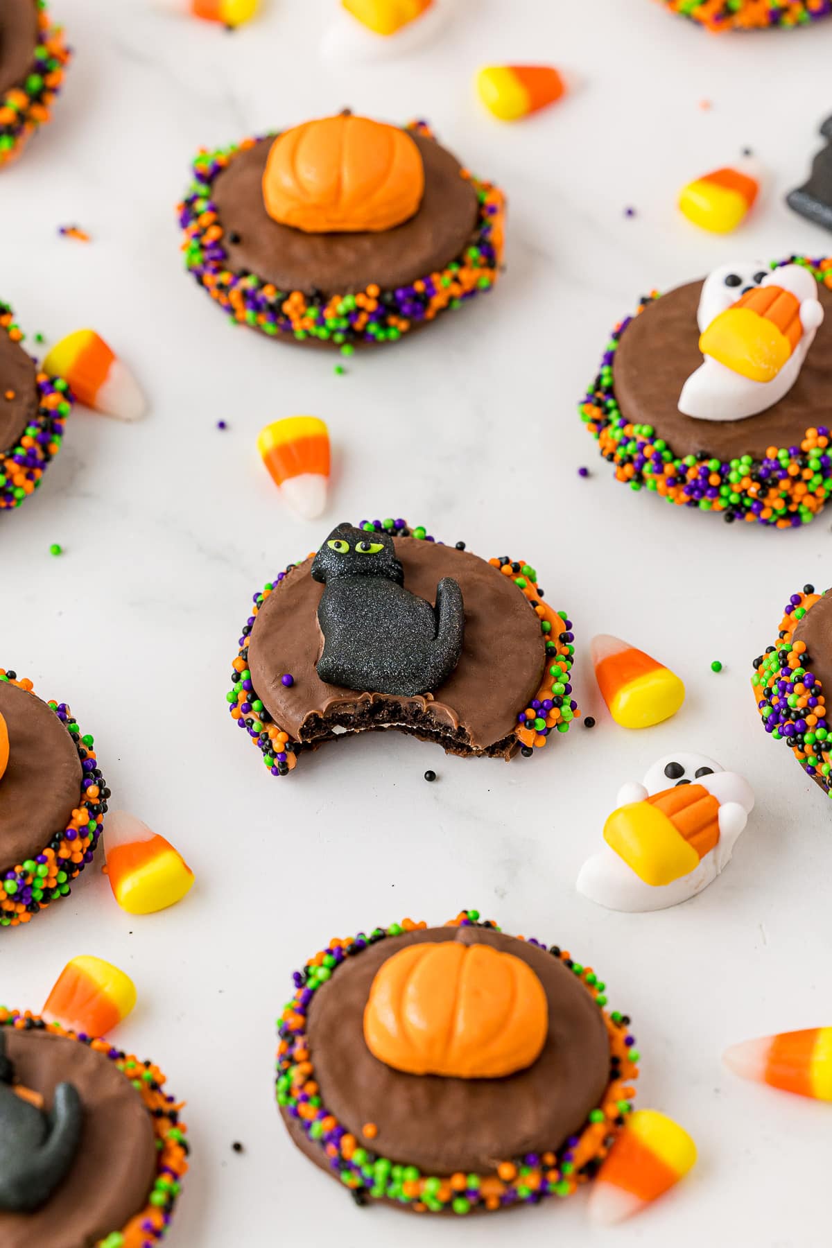 Chocolate covered oreos with halloween decorations on a white marble countertop, scattered candy corn. 