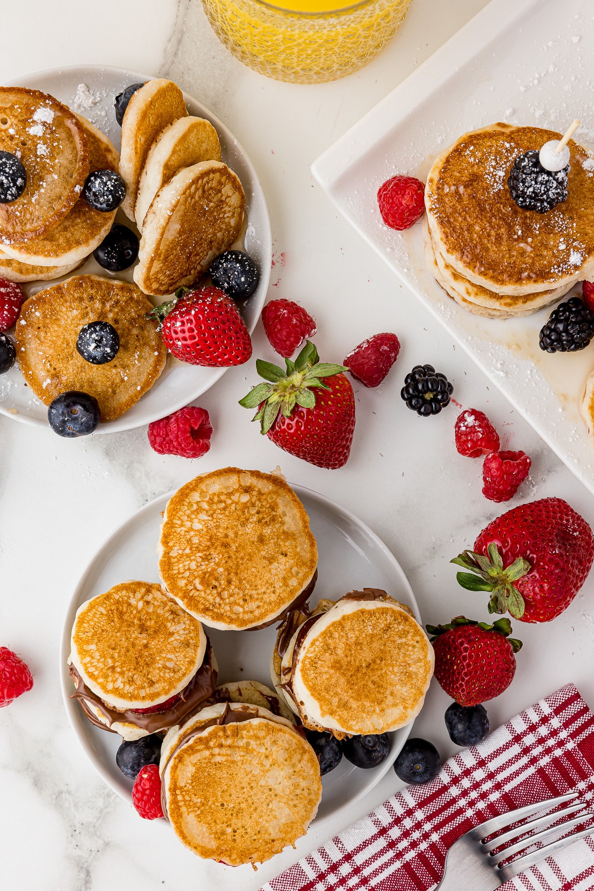 overhead photo of mini pancakes on serving platters with a fork and red and white napkins