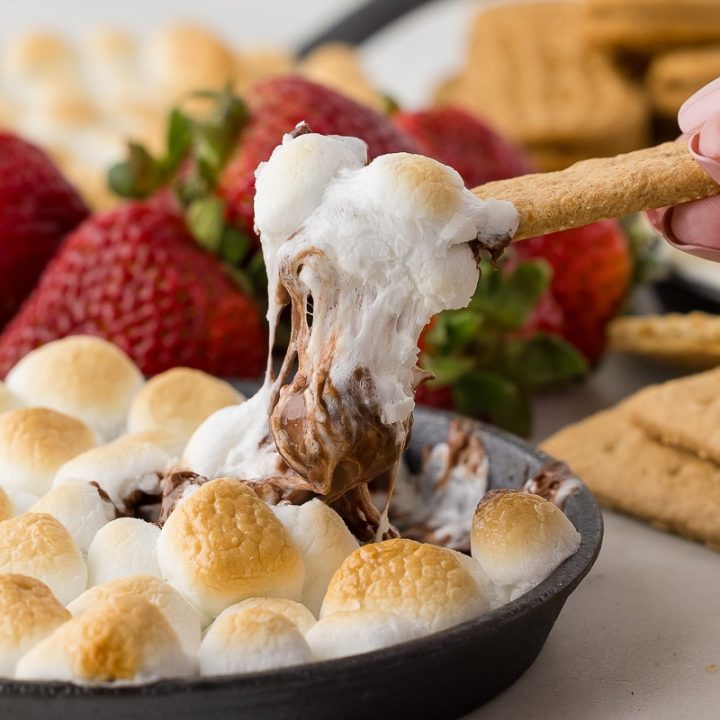 graham cracker dipped in chocolate and toasted marshmallows with strawberries and square pretzels in the background.