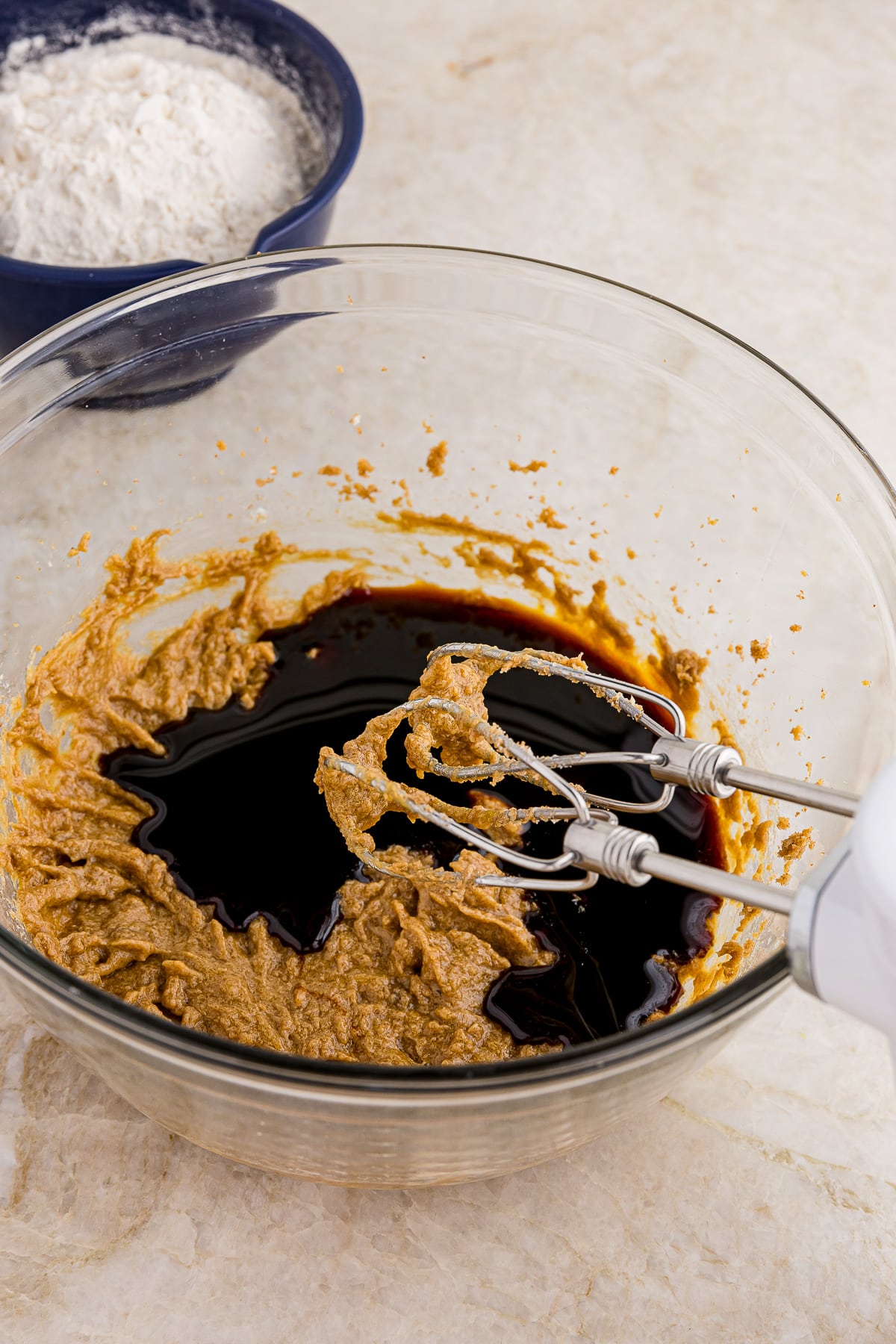 creamed butter and brown sugar in a glass bowl with mixing beaters and molasses for gingerbread cookie recipe