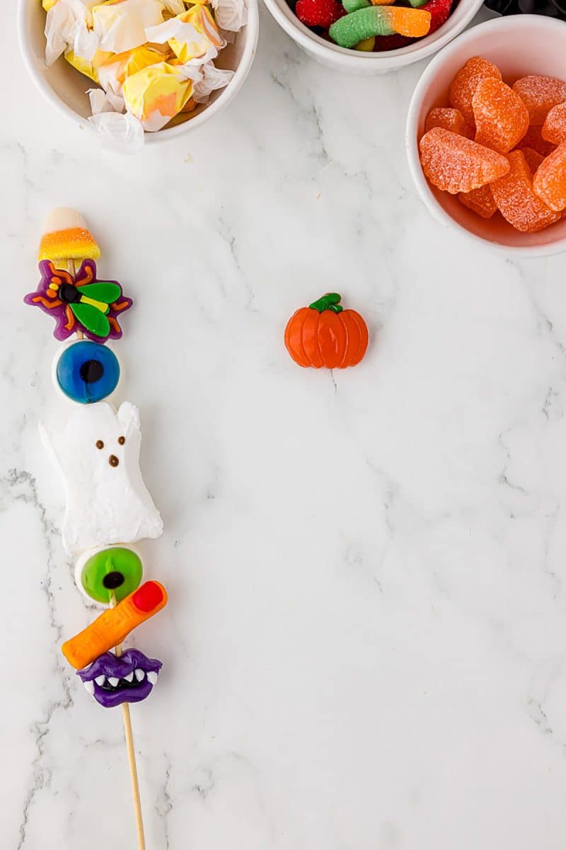 candy skewer, three bowls of jelly candies, and the first jelly candy pumpkin on a white countertop