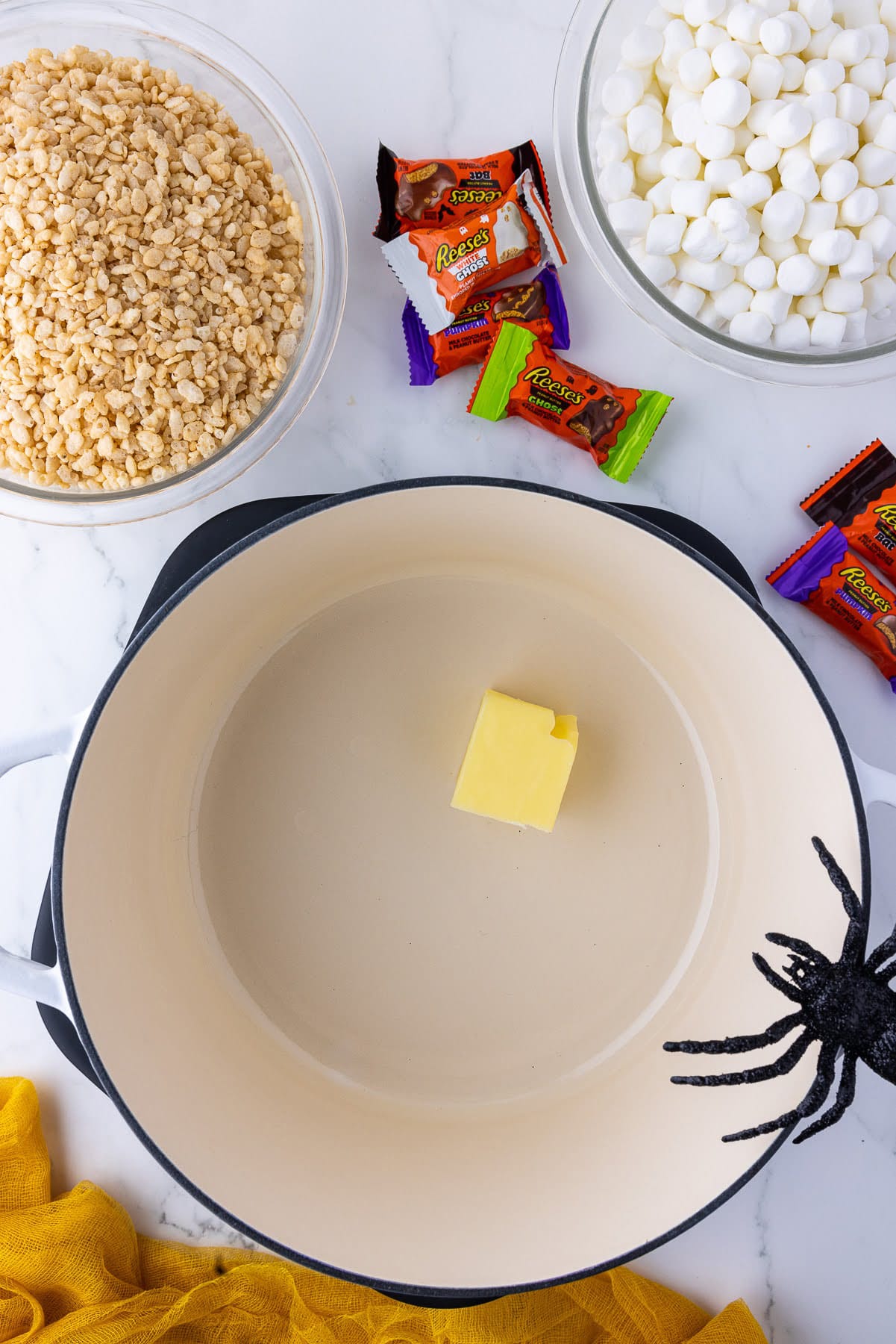 butter in a pot with a spider on the side and wrapped candies, a bowl of rice crispies and a bowl of mini marshmallows