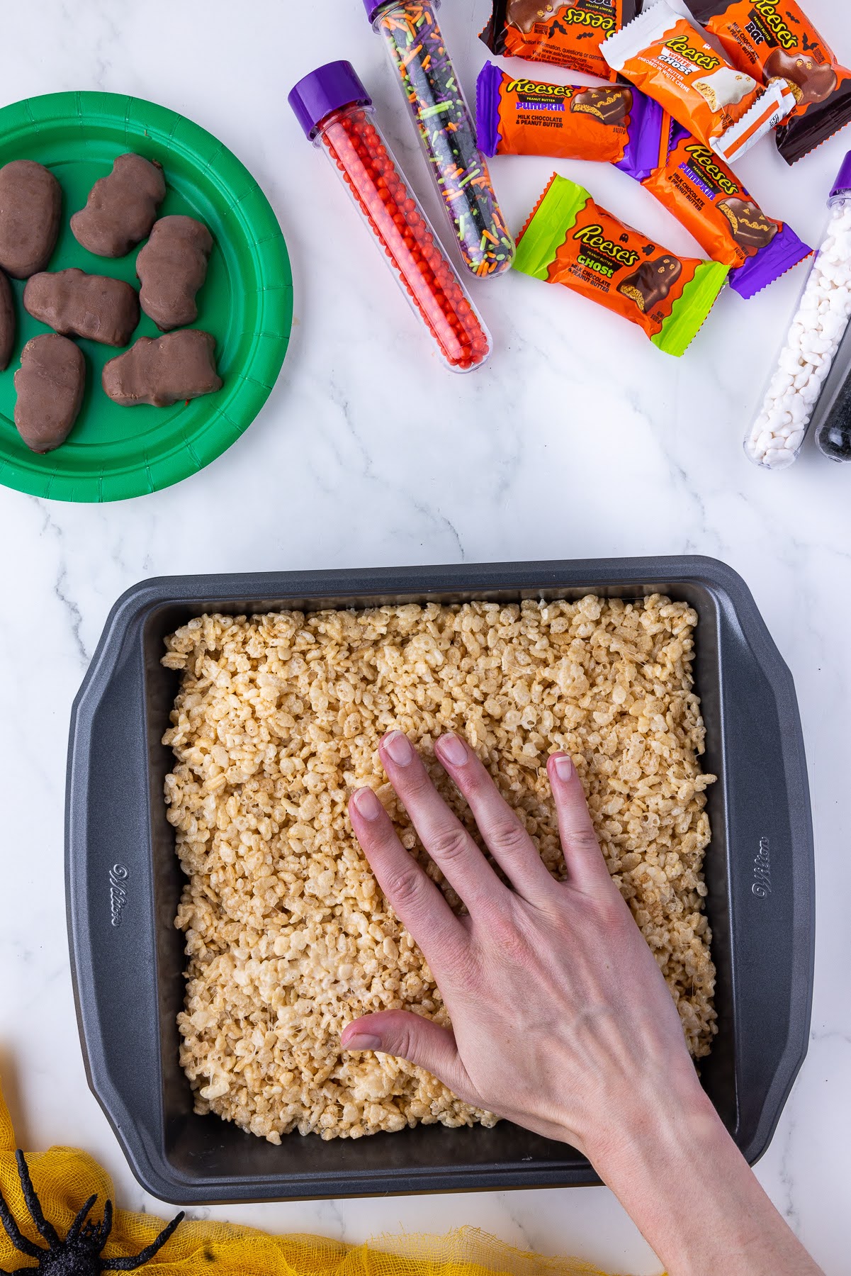 flattening rice crispies into a square pan with candies in the background