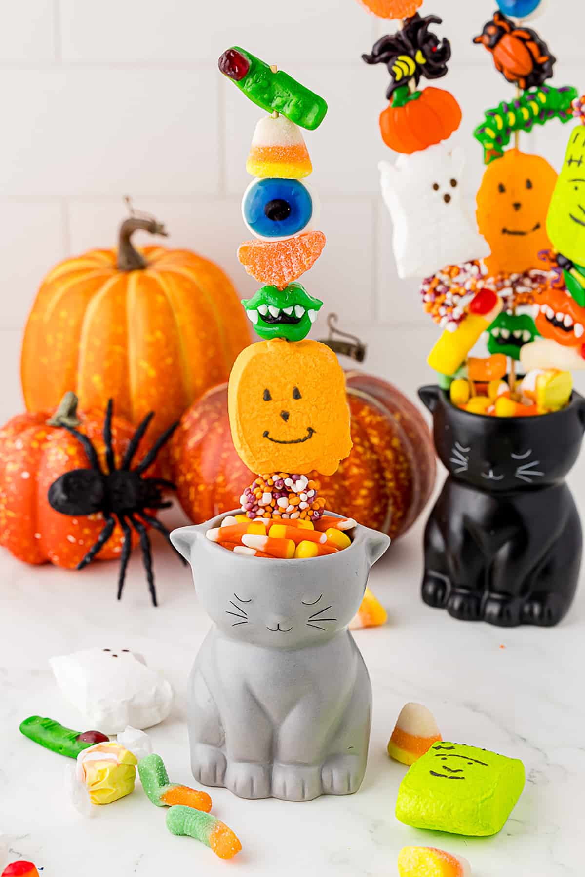 cat planter filled with candy corn and candy skewers of halloween candy kabobs on a white countertop with pumpkins in the background