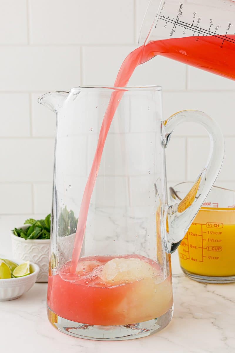 glass measuring cup with grapefruit juice pouring into glass pitcher
