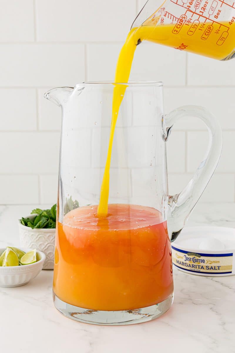 pyrex cup pouring orange juice into a glass pitcher