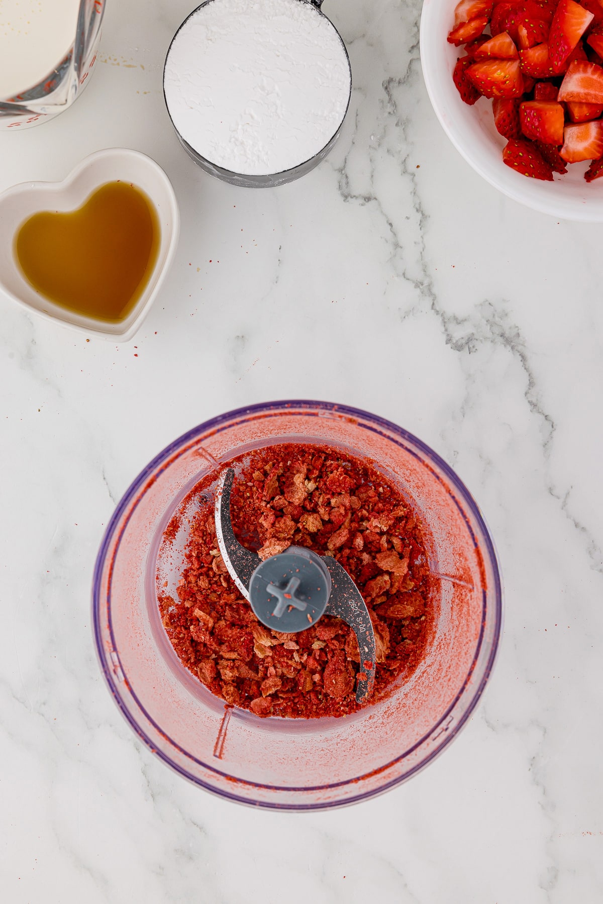 mini chopper filled with freeze dried strawberries on a white marble counter