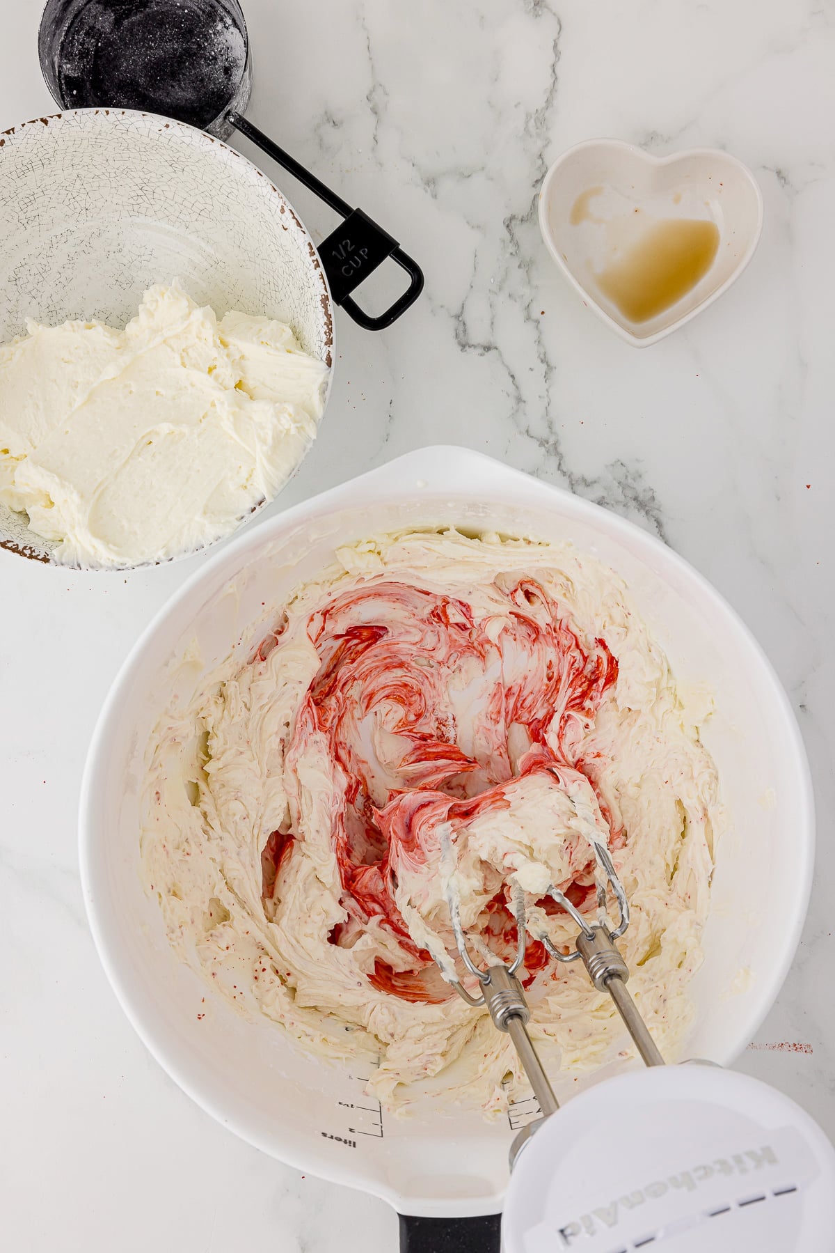 cream cheese mixture with freeze dried strawberries being mixed in a white batter bowl with a hand held mixer