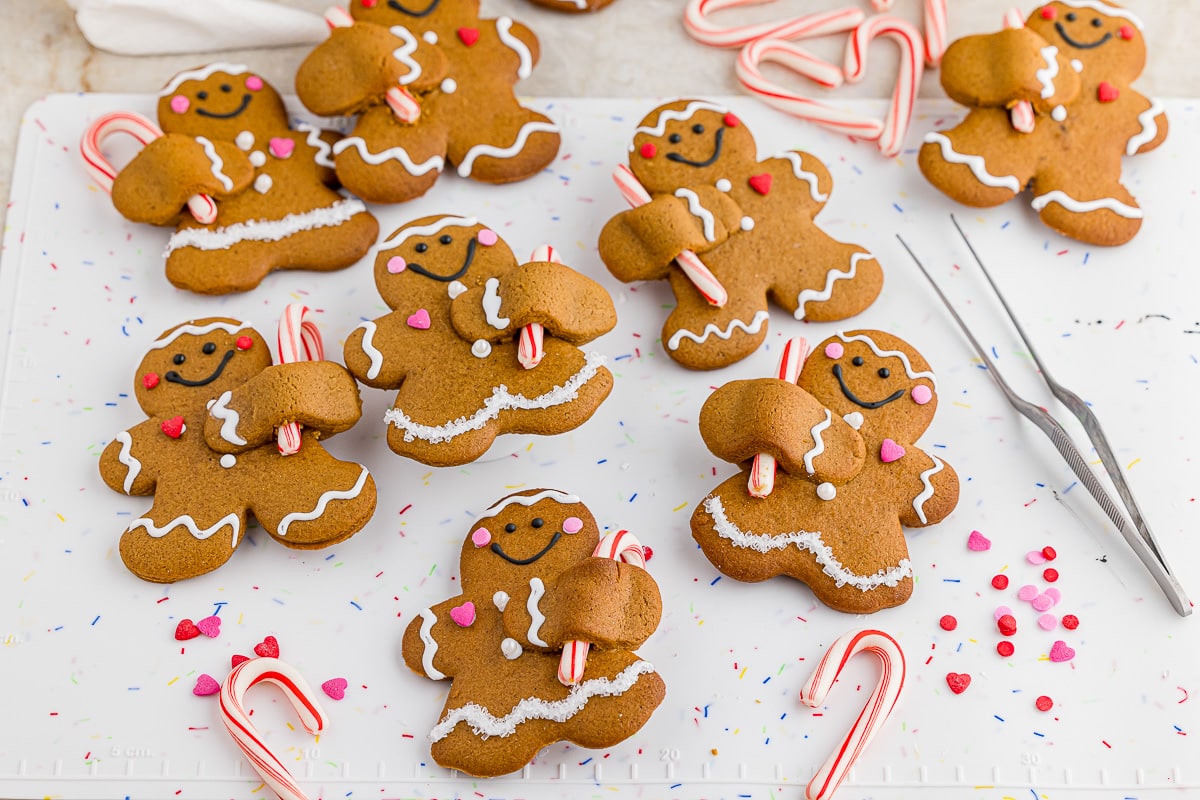 8 decorated gingerbread men on a wilton decorating mat with food tweezers and candy canes