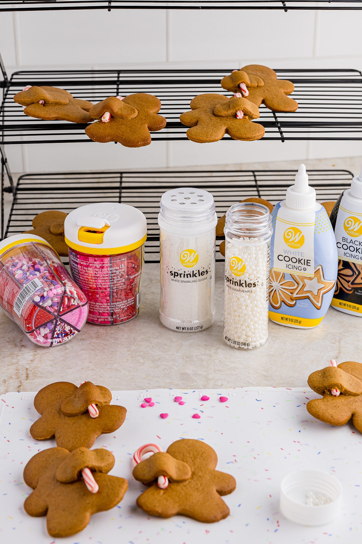 witlon sprinkles and cookie icing on a white countertop with a tri fold cookie sheet and undecorated gingerbread men