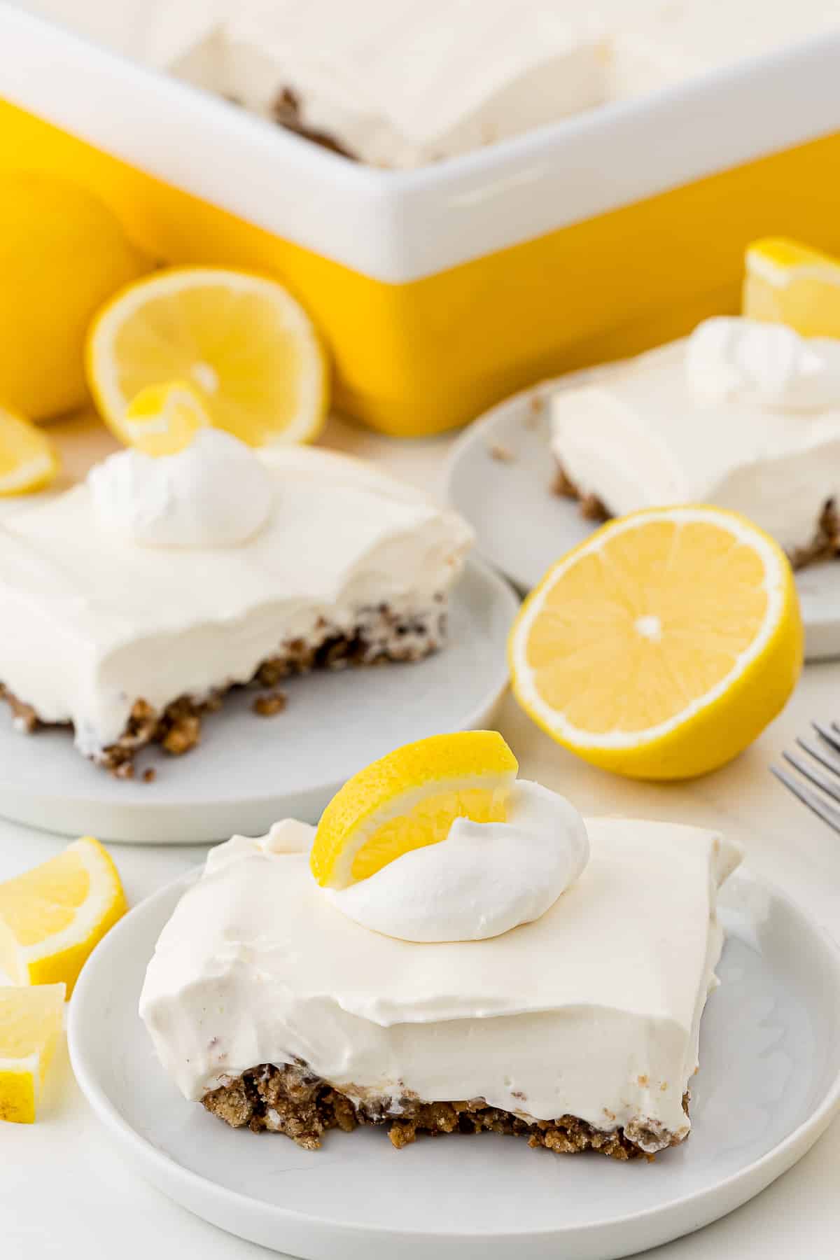 Lemon pie slices on plates with a large dish pie in the background