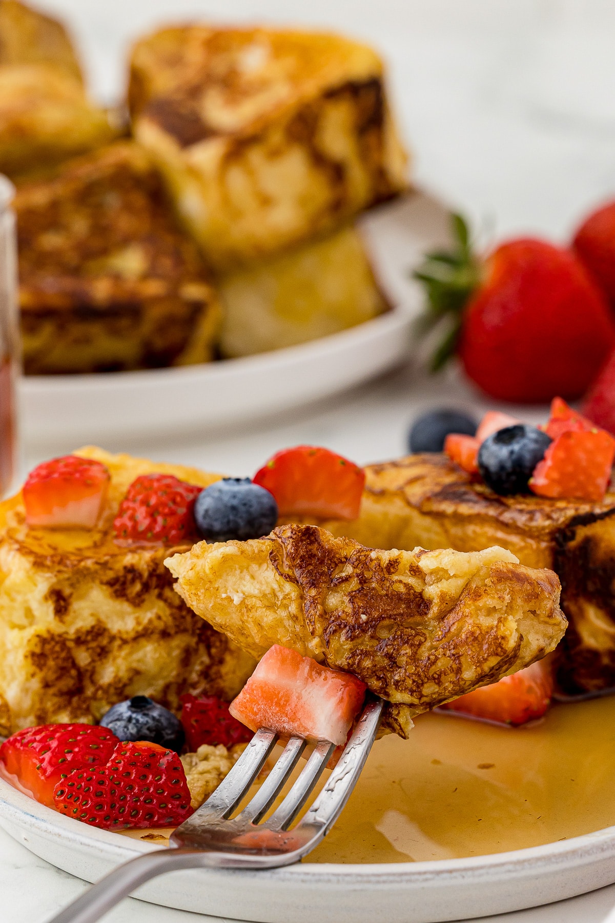 bite of french toast and strawberry on a fork with more french toast and berries on a plate