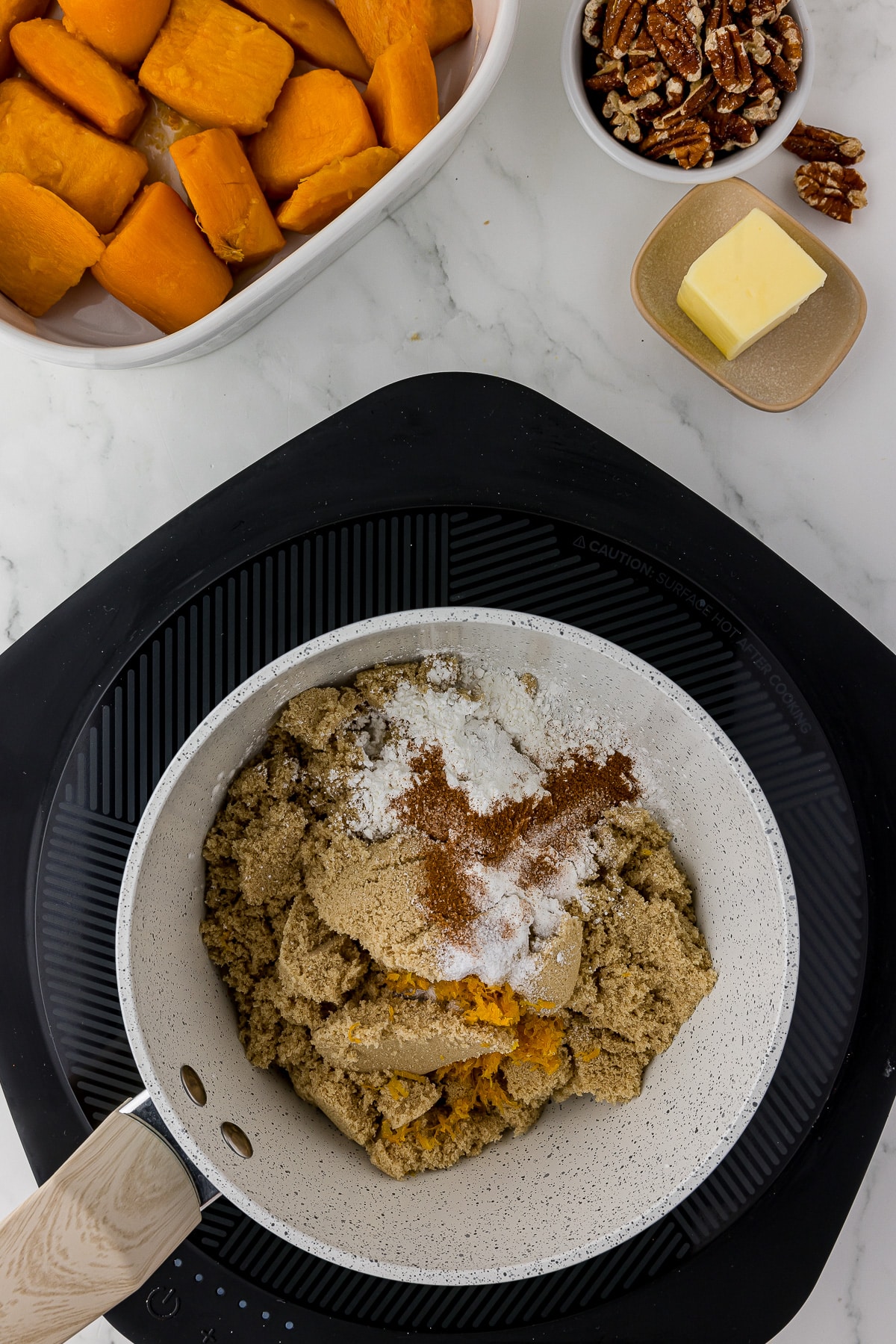 heating plate with a saucepan that has brown sugar, cornstarch, orange zest, and salt inside. Butter, pecans, and sweet potatoes in the background