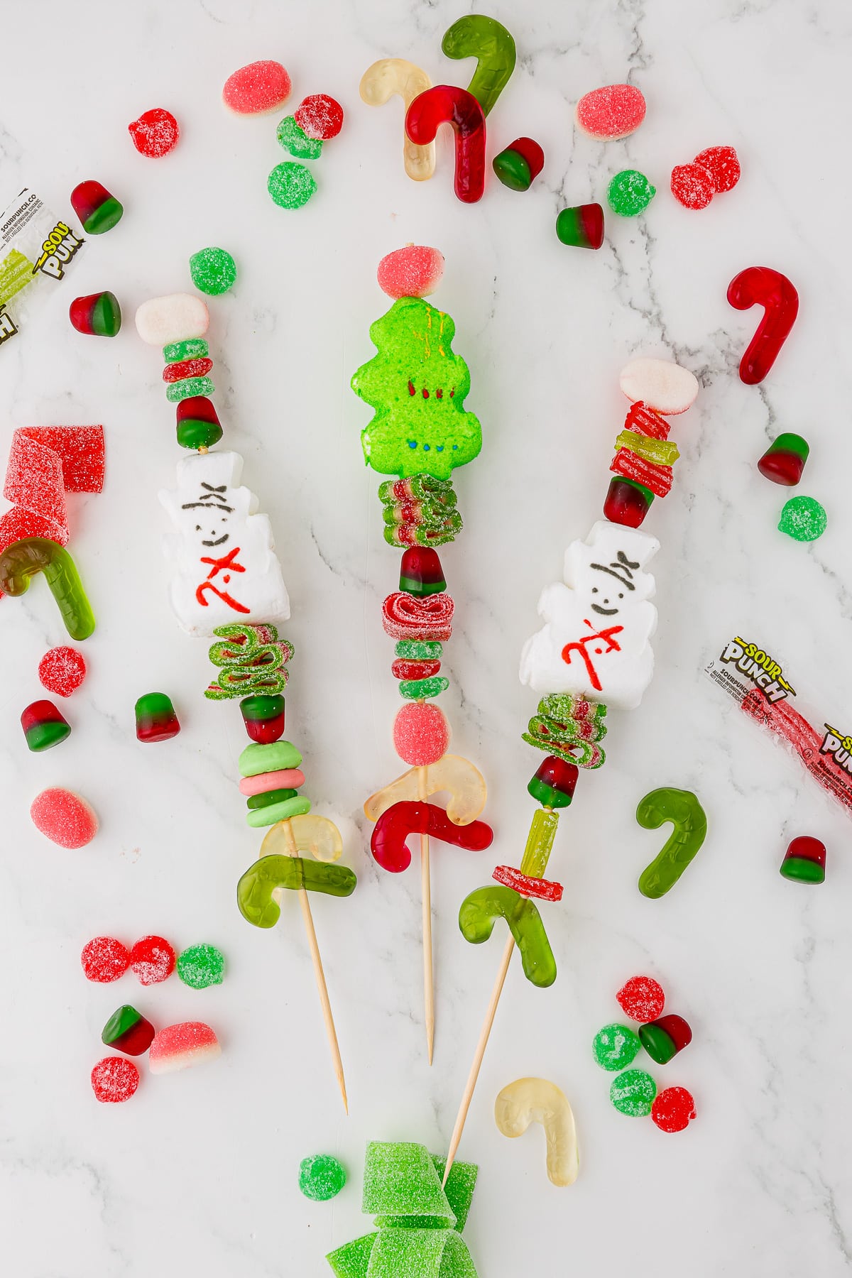 Skewers with assorted gummy Christmas candies on a shite countertop