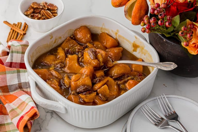 apricot yams in a white casserole dish with a bowl of pecans, cinnamon sticks on the countertop and a plaid autumn napkin with two small white plates and two forks