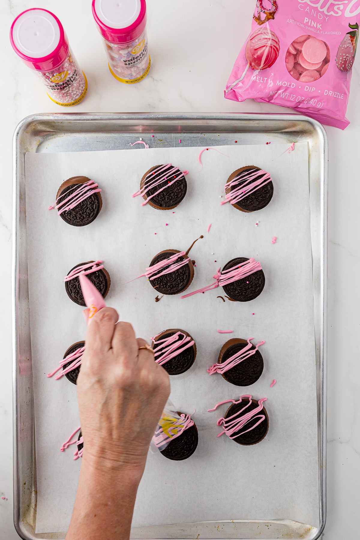 12 reese's oreos decorated for valentine's day with pink chocolate sitting on parchment paper with sprinkles and Wilton pink cany melts on a white counter