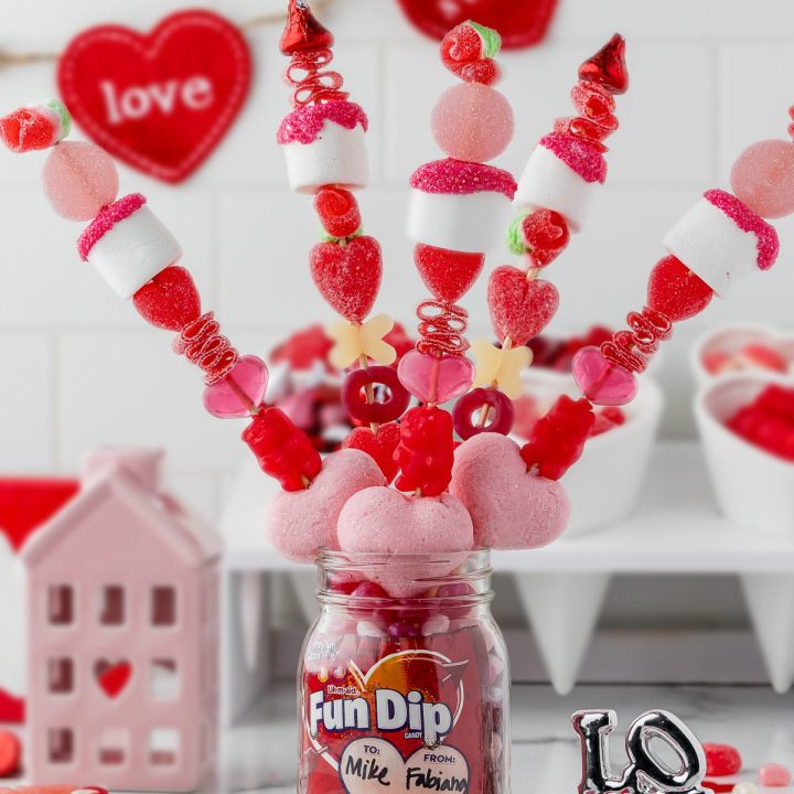5 valentine's day candy kabobs in a mason jar with fun dip and heart shaped accessories and a LOVE silver statue and pink ceramic house