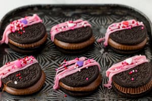 six reese's oreos with pink melted chocolate and valentine's day sprinkles on a cookie sheet