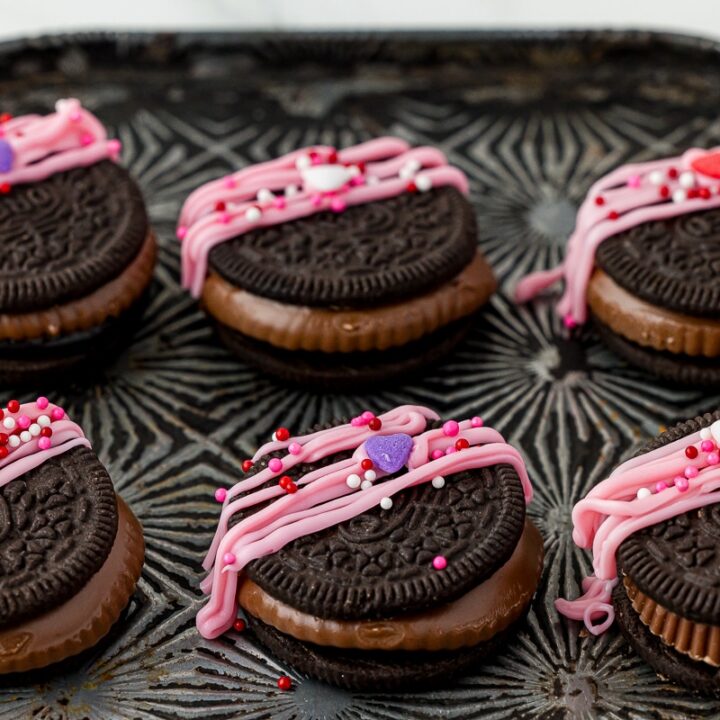 six reese's oreos with pink melted chocolate and valentine's day sprinkles on a cookie sheet