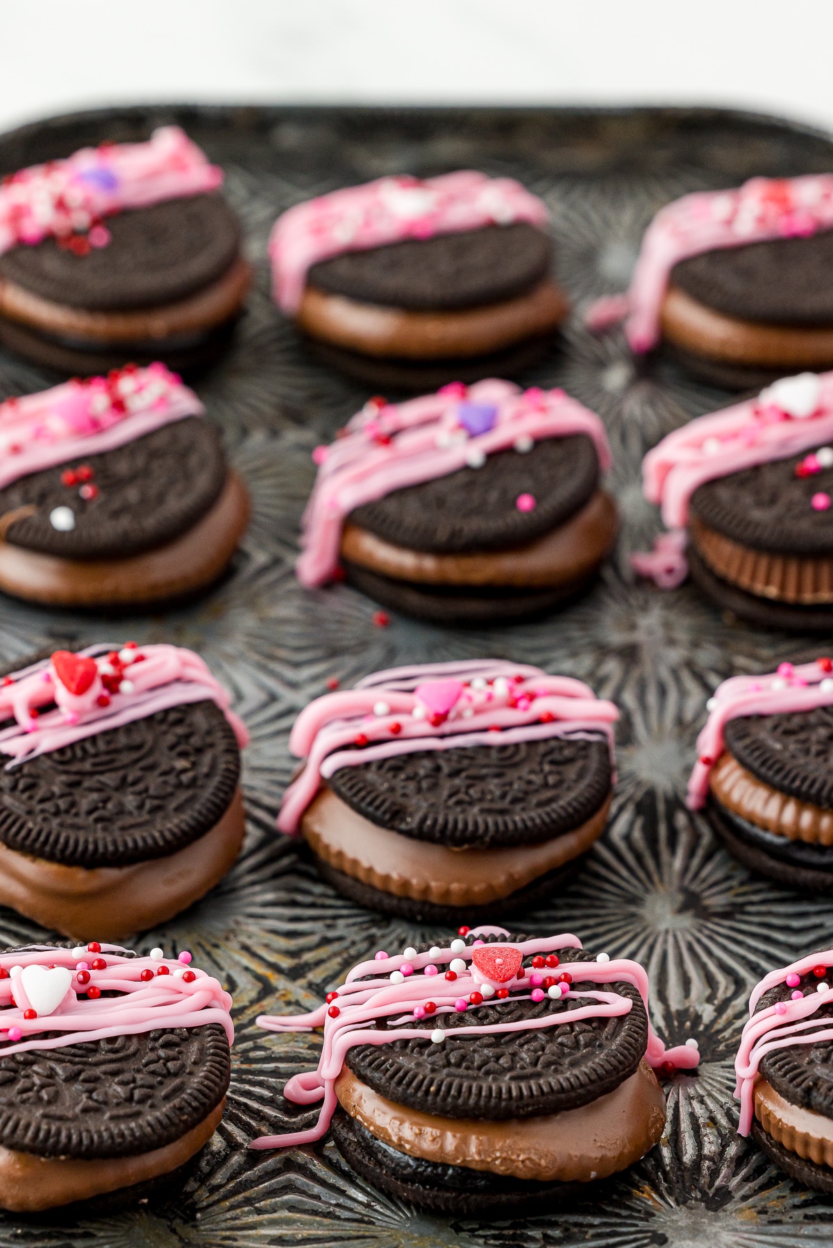 12 reese's oreos decorated for valentine's day with pink chocolate sitting on an antique metal pan.