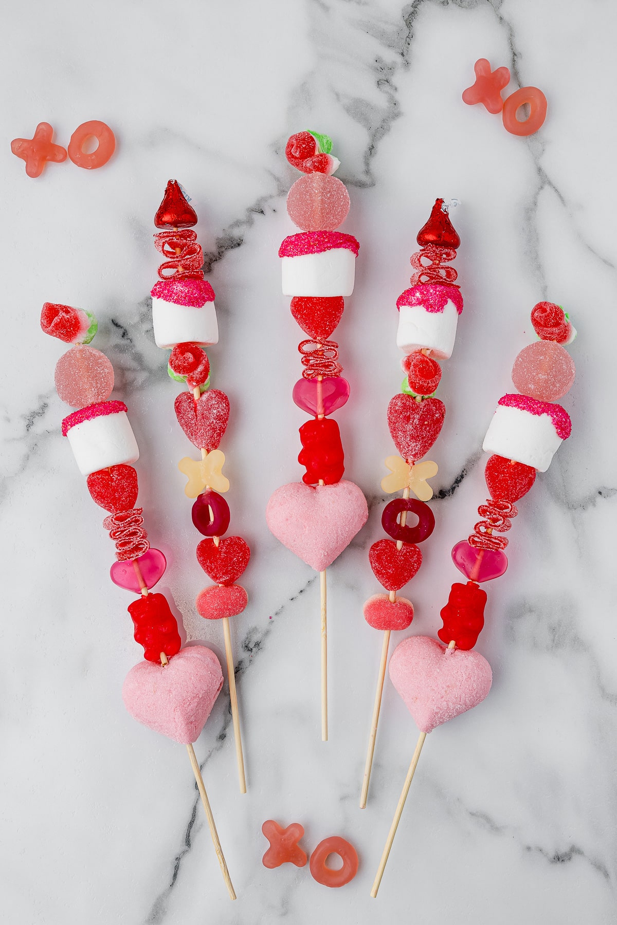 5 valentine's day candy kabobs on a white marble countertop with candy x's and o's
