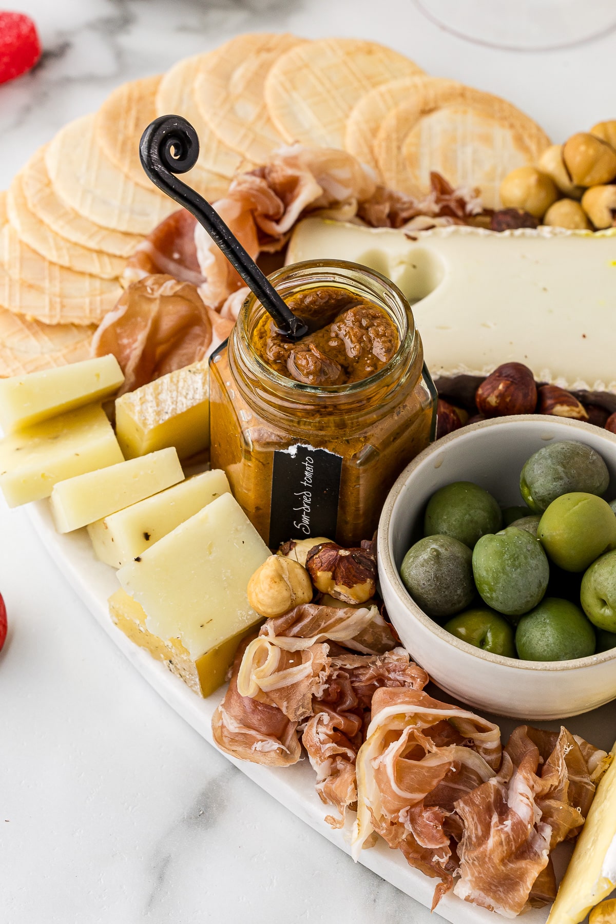 Jar of dipping sauce, olives in a bowl and cheese and meats on a party platter