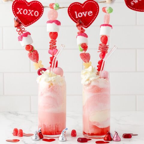 two strawberry soda floats on a white countretop with a valentine's day garland