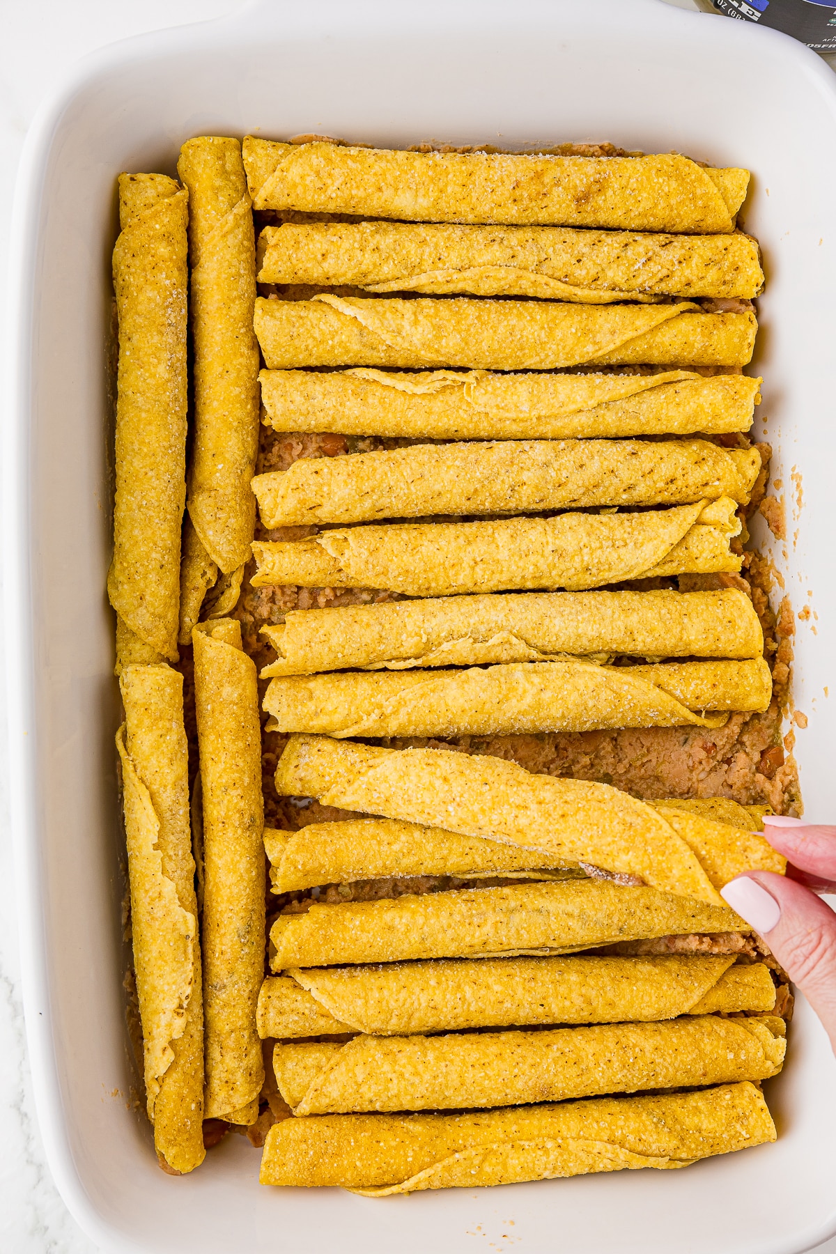 layered frozen taquitos in a 9x13 white dish