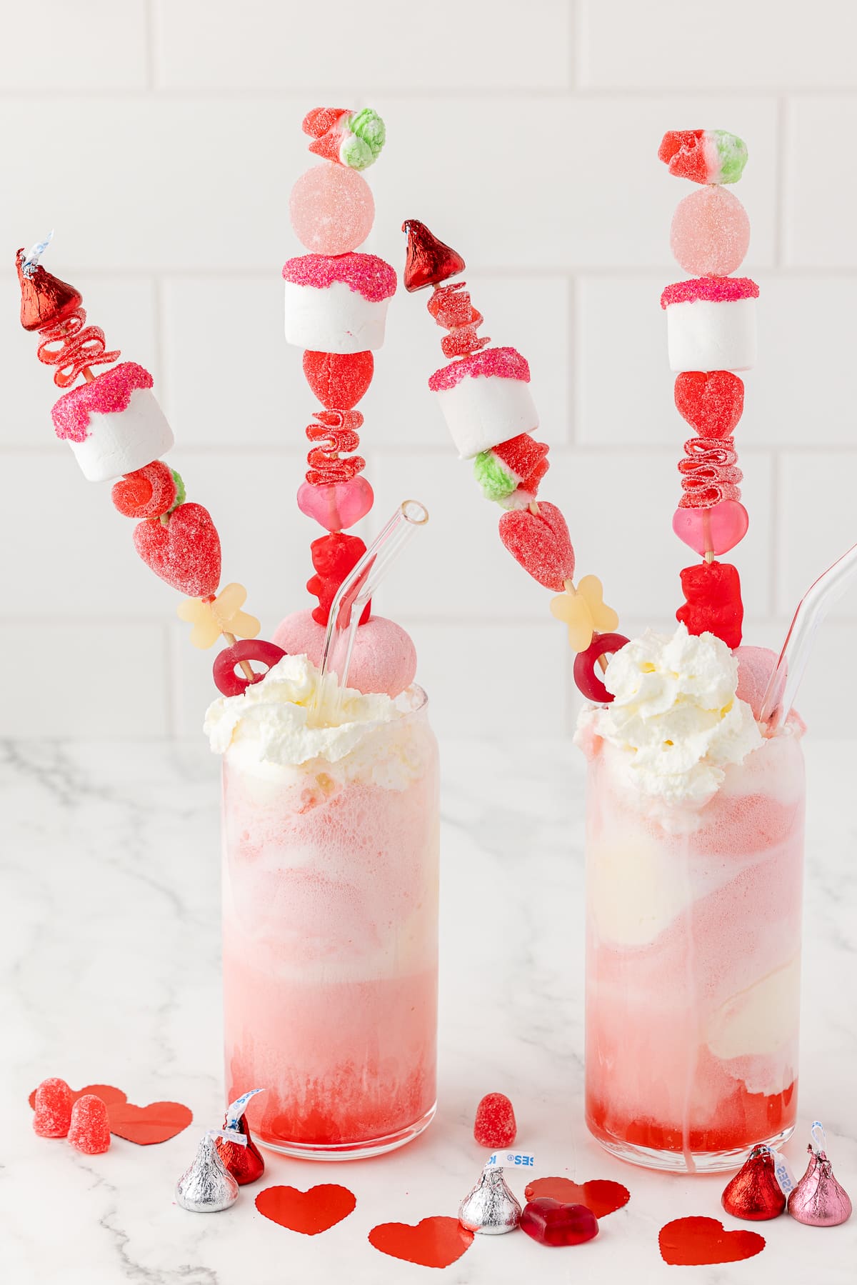 two strawberry soda ice cream shakes on a white countertop with red and pink kabobs