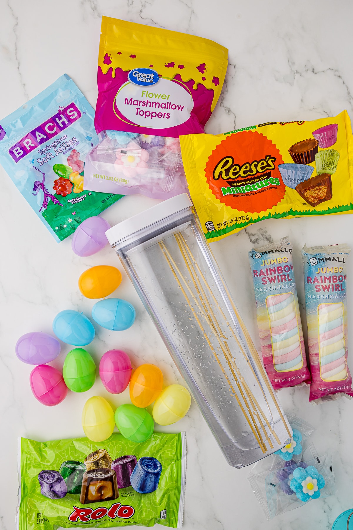 ingredients for easter candy kabobs, including great value flower marshmallow toppers, reese's miniature peanut butter cups, yummall jumbo rainbow swirl marshmallows, bamboo skewers in water, fillable plastic easter eggs, and easter rolos