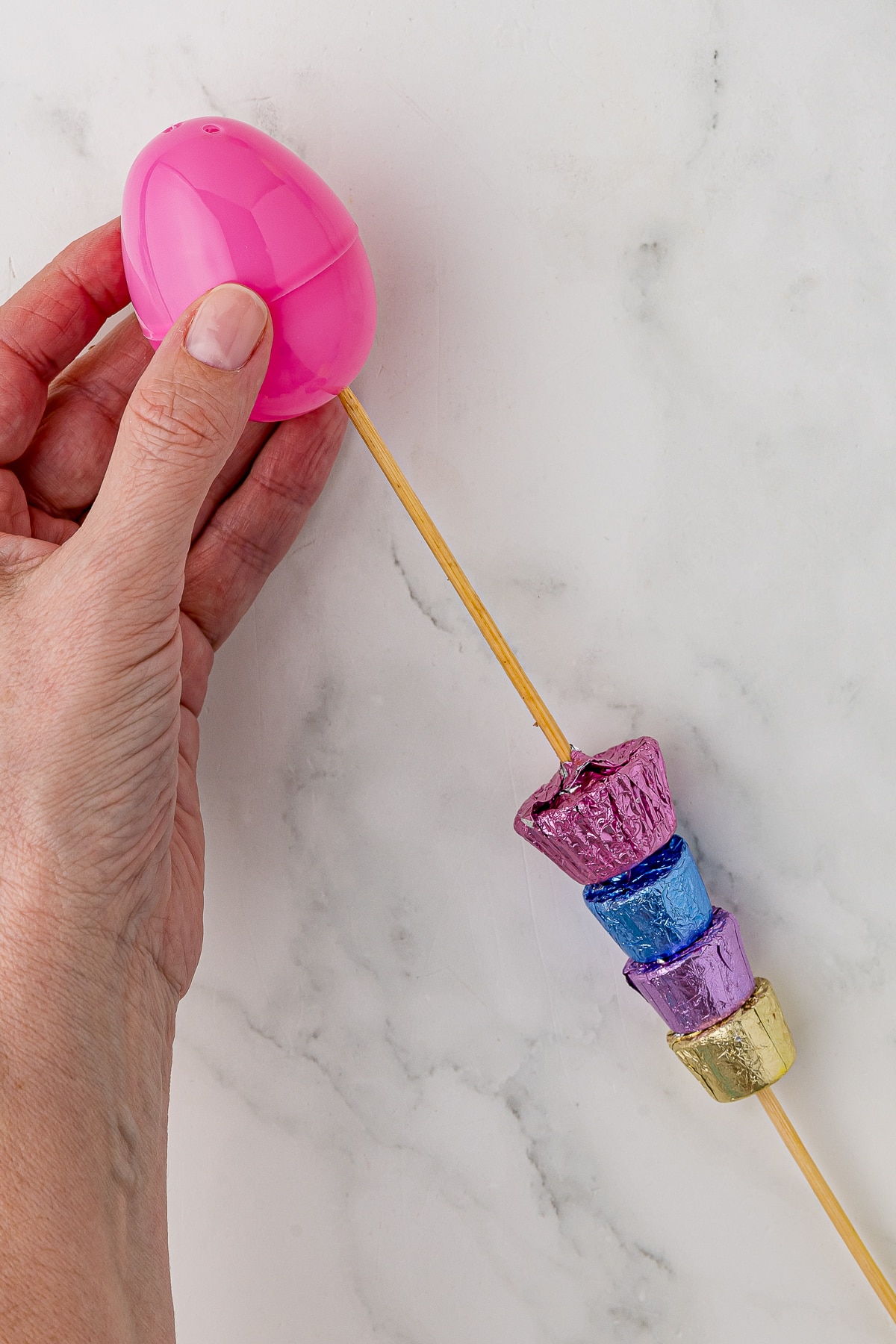 putting a skewer through a pink plastic fillable egg. The skewer has a reese's peanut butter cup and three rolos already on the skewer