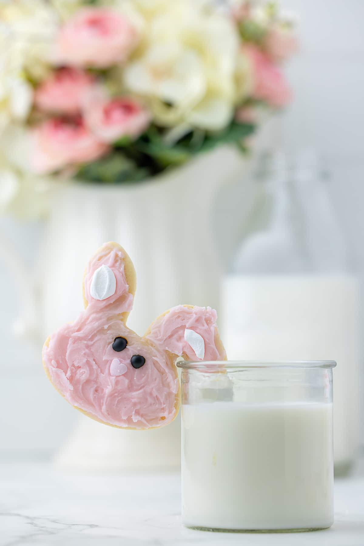 Easter bunny sugar cookie with ear hooked on to side of glass of milk