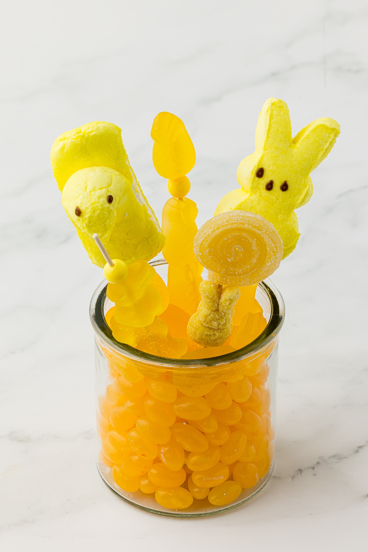Yellow jelly beans in a small jar with yellow candy kabobs made with yellow gummy candy bought at Five Below on a white countertop.