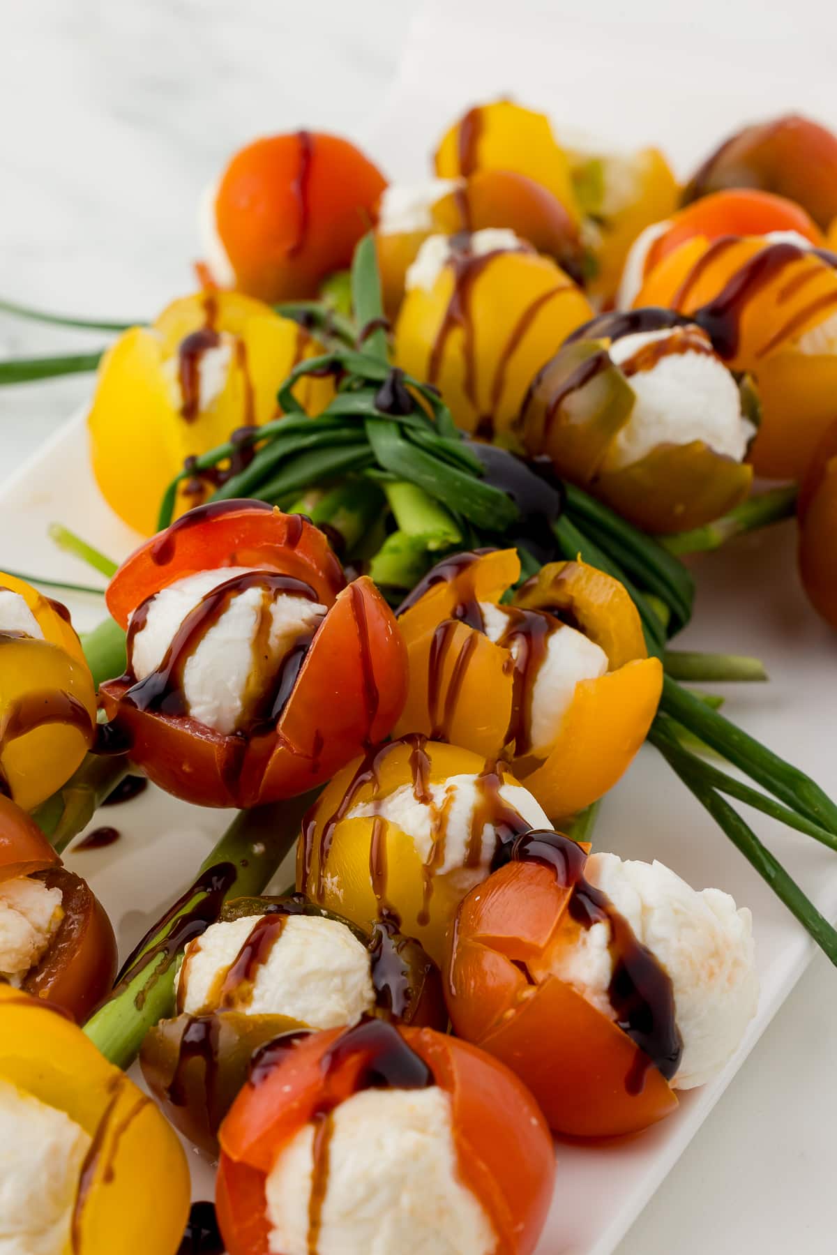 bouquet of cherry tomato tulips filled with mozzarella and drizzled with balsamic glaze tied with chives on a white platter