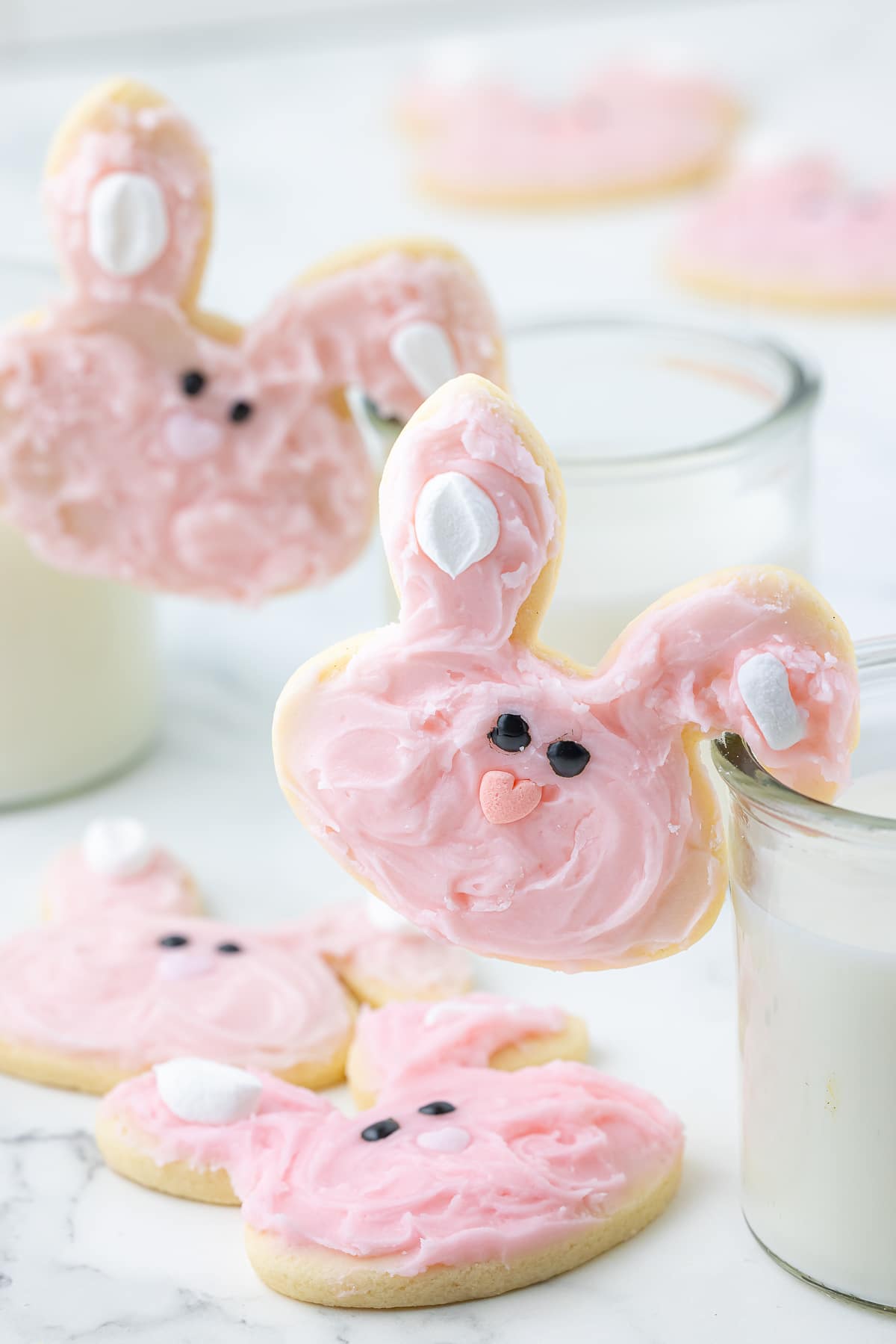 pink frosted sugar cookies with glasses of milk
