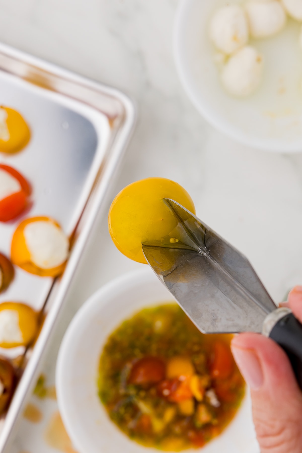 yellow cherry tomato being pierced with a v shaped garnish knife