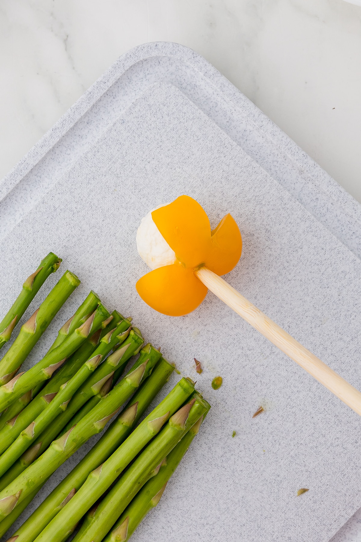 asparagus spears on a cutting board, a skewer piercing the bottom of a yellow cherry tomato