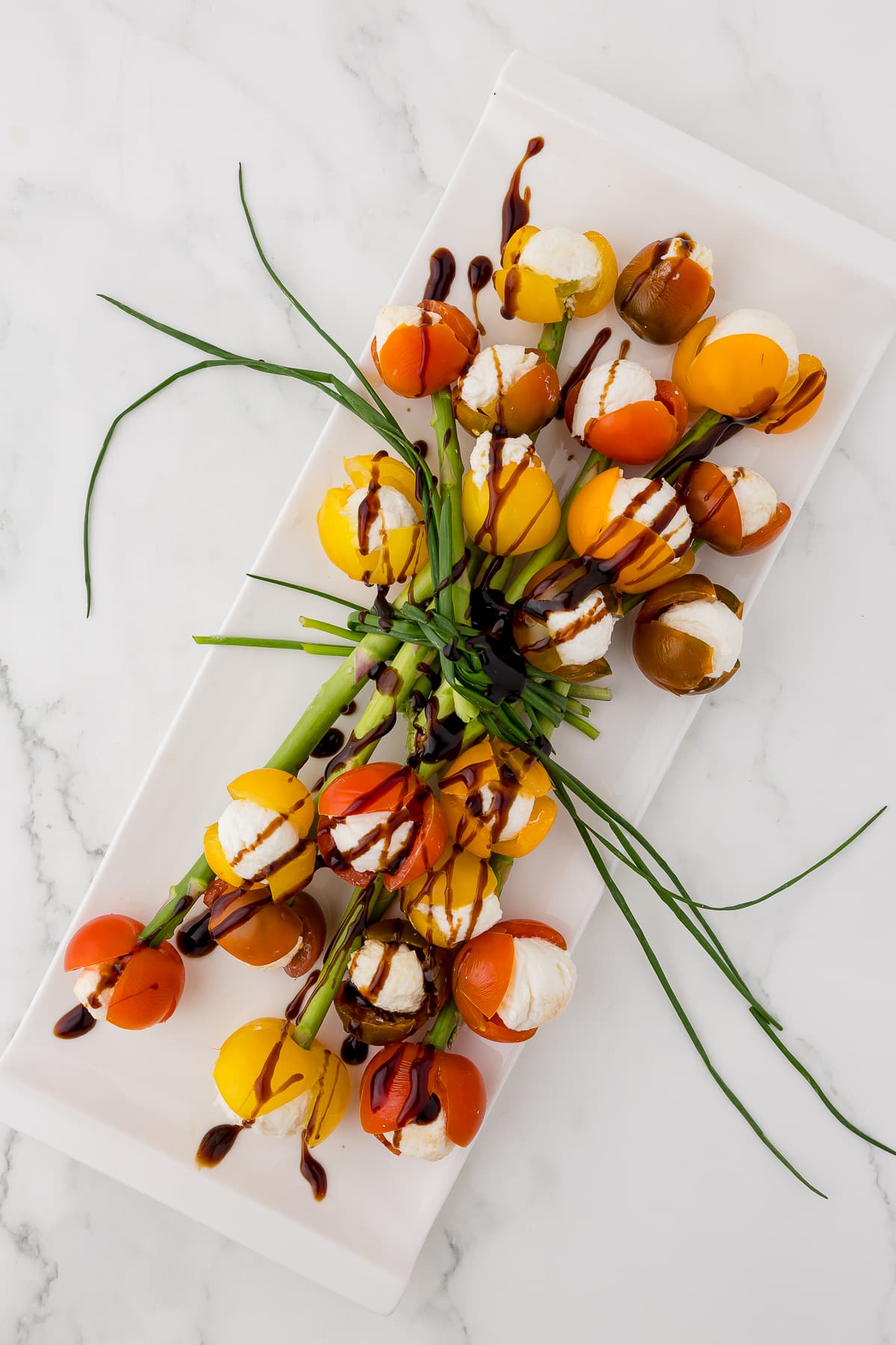 tomato tulip bouquet drizzled with balsamic glaze on a white platte that has been turned at a diagonal on a white counter top