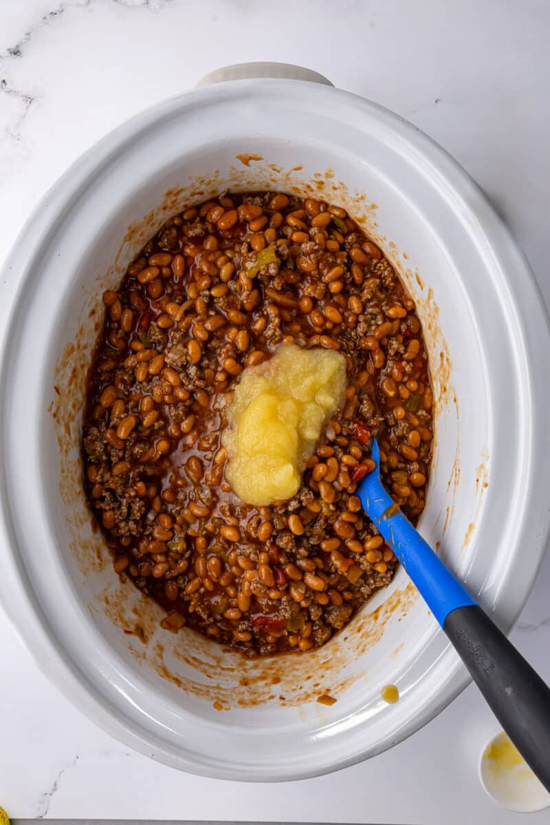 applesauce over the baked bean mixture with a blue spatula