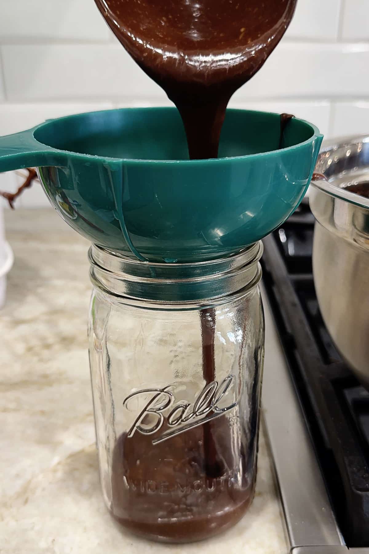 transferring chocolate sauce into a ball canning jar using a green funnel