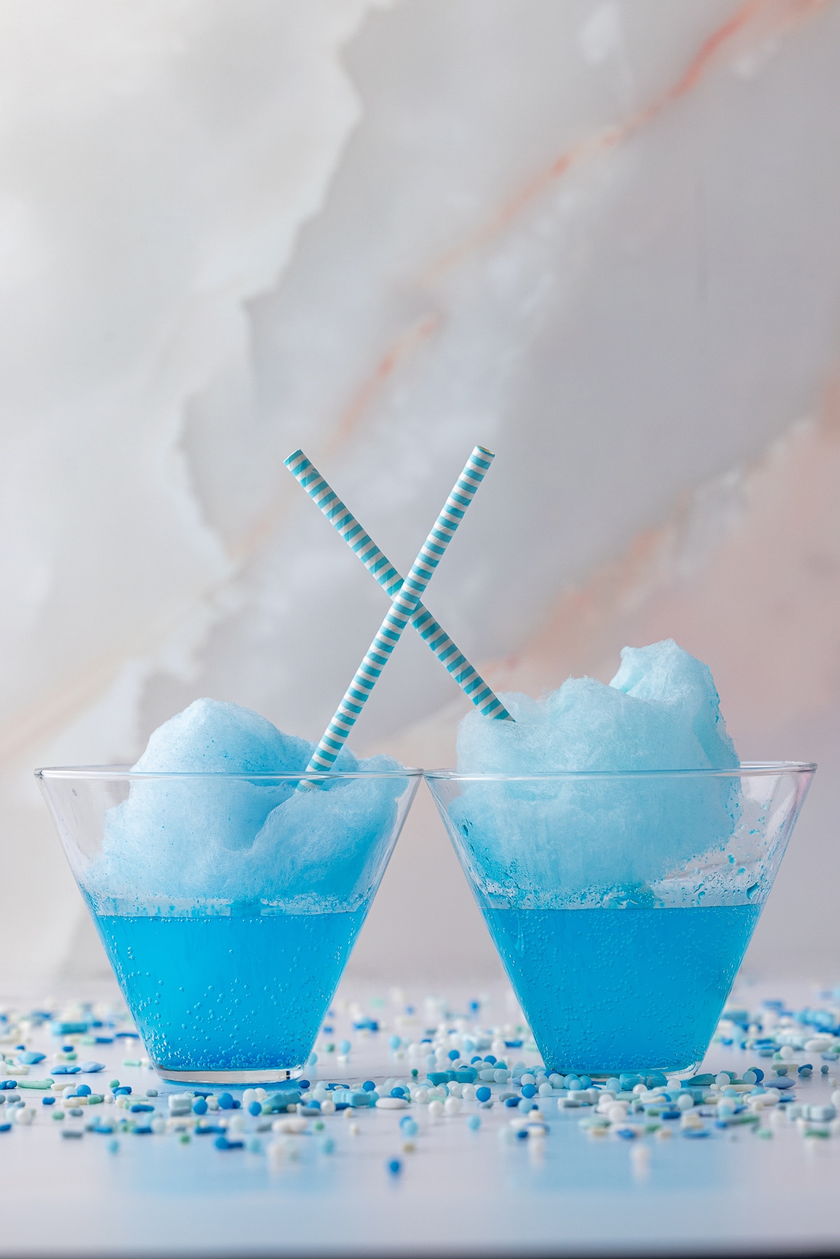 blue soda in a glass topped with blue cotton candy, blue straws, with wilton blue spinkles on the counter