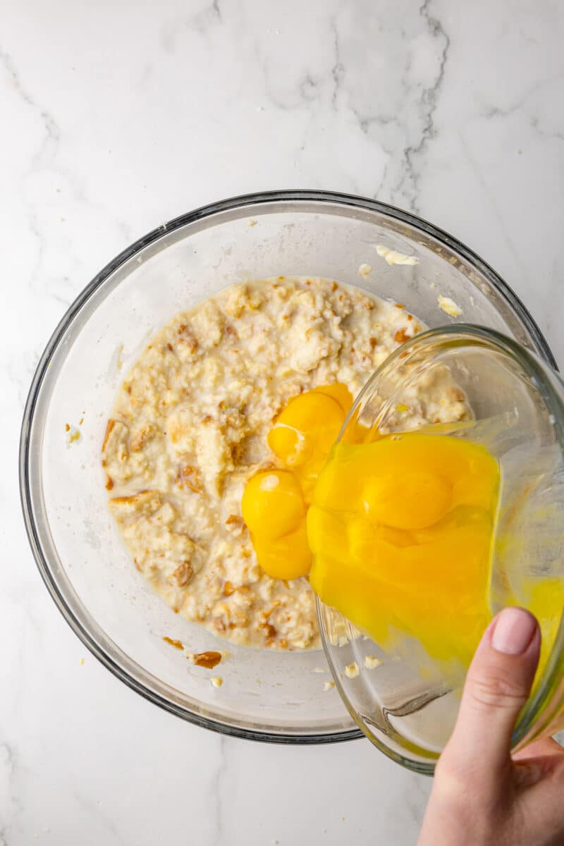 pouring egg yolks into a glass bowl with bread mixture