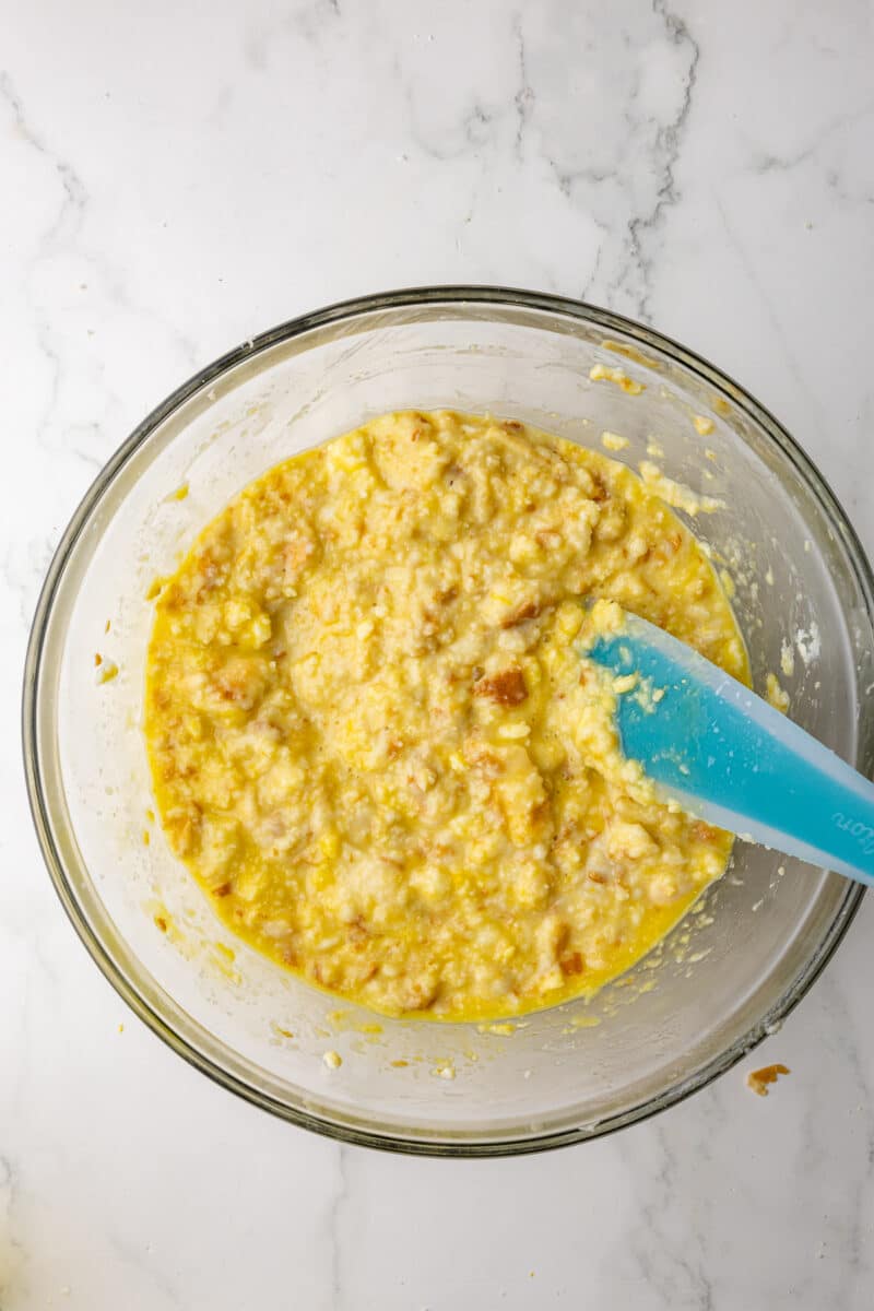 bread and egg mixture in a glass bowl with a blue spatula