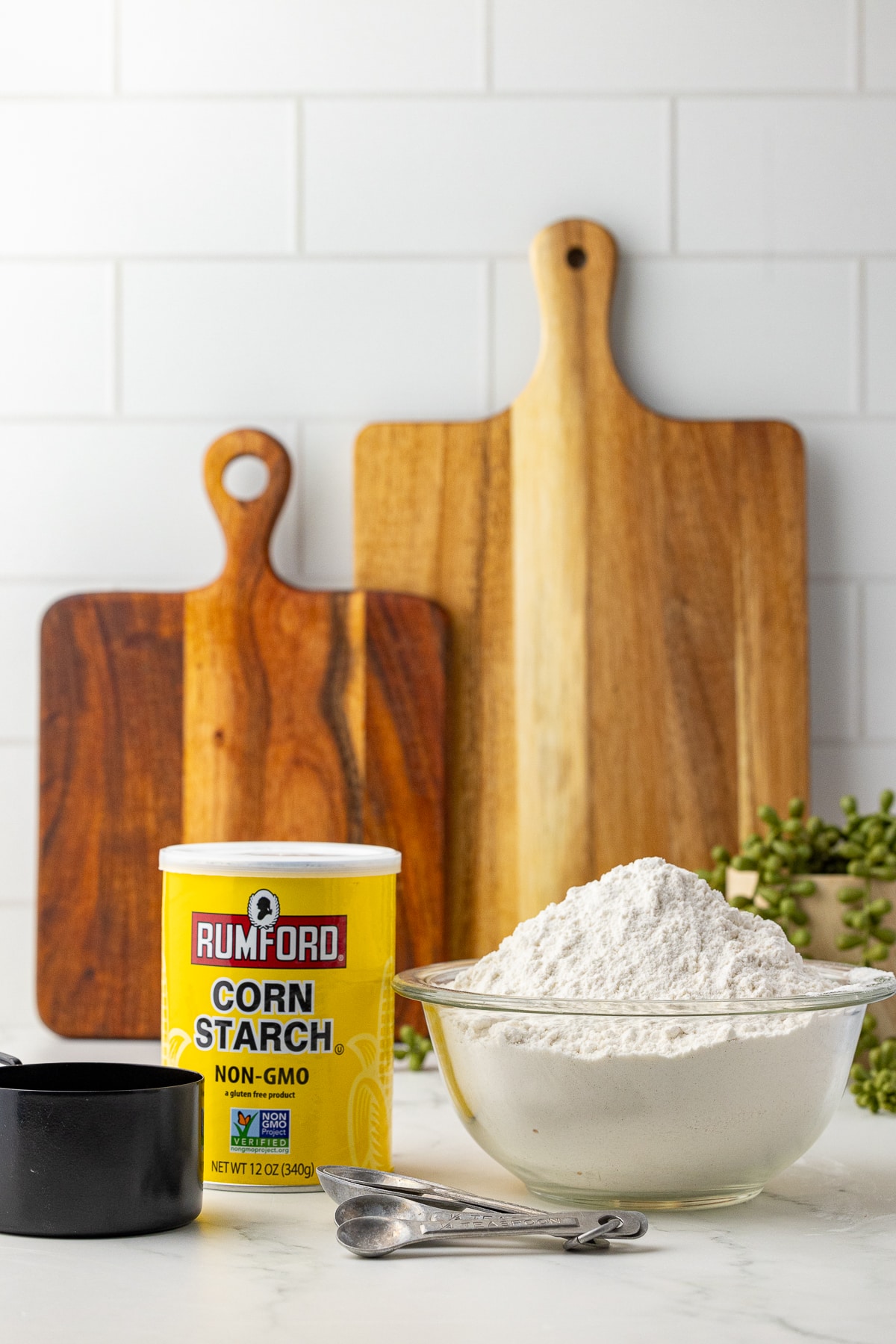 corn starch, a bowl of flour, two cutting boards, a measuring cup and a set of measuring spoons on a white counter with white subway tile backsplash