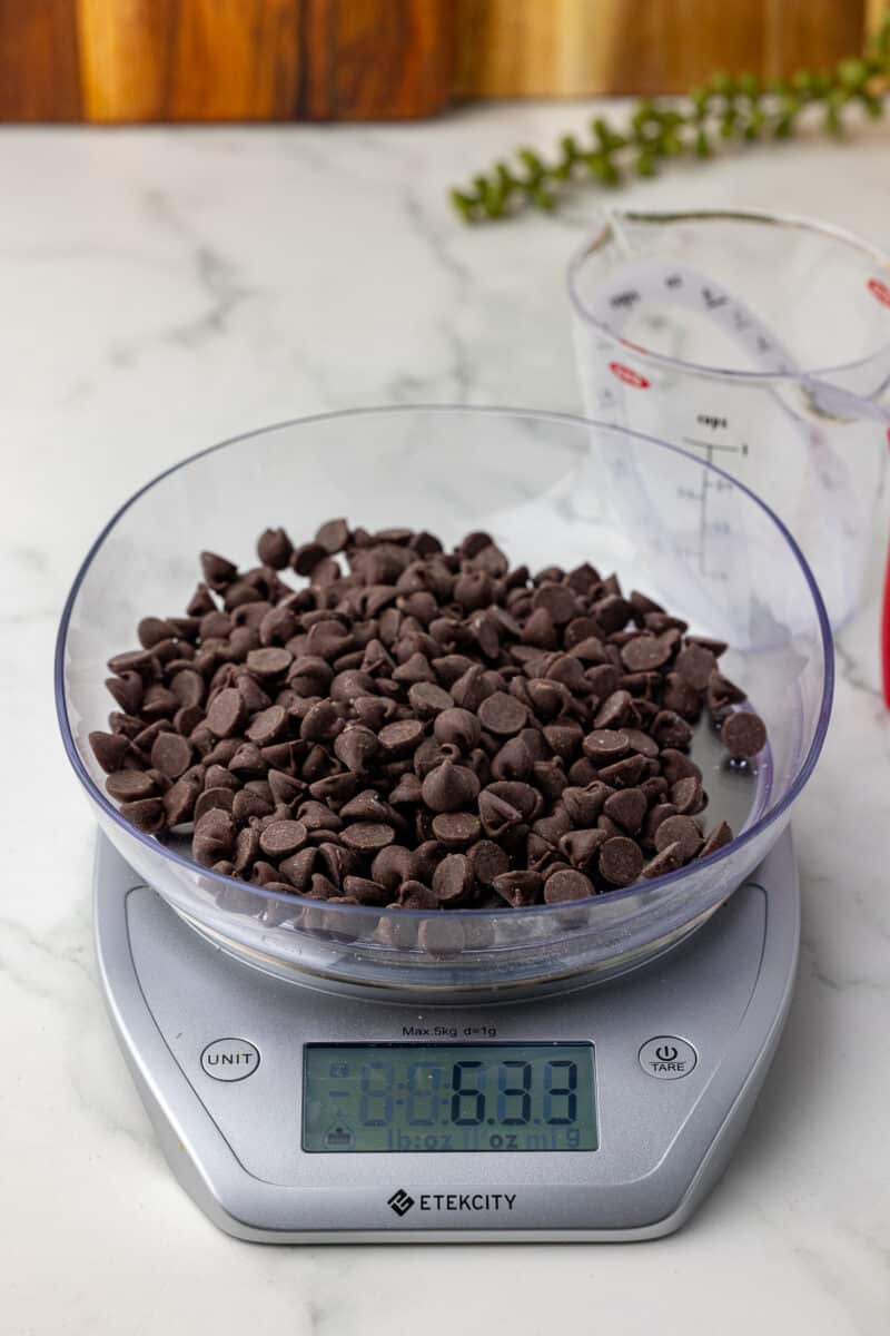 one up of chocolate chips on a kitchen scale with an oxo liquid measuring cup in the background