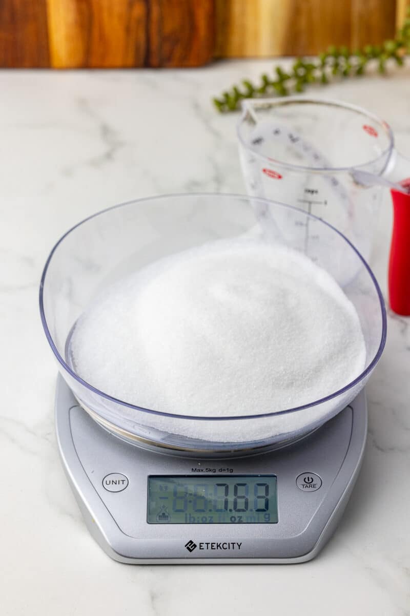 one cup of sugar on a scale with an oxo liquid measuring cup in the background
